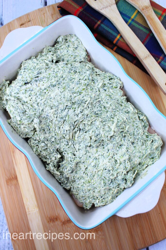 A layer of cheese and spinach is spread in a casserole dish. 