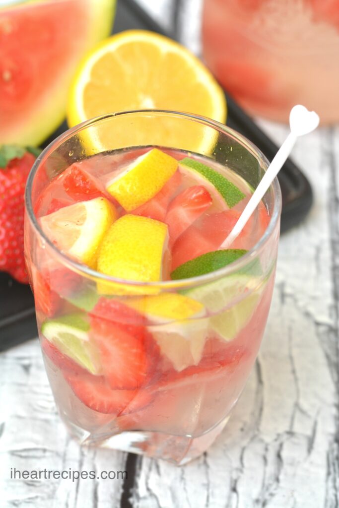 A clear glass filled with After Holiday Detox Water. Fresh lemon, lime and strawberries float in a pale pink liquid. 