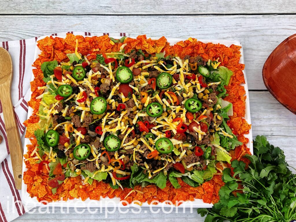Tender meat, fresh veggies and creamy cheese arranged on a bed of crunchy Doritos served on a large rectangular platter. 