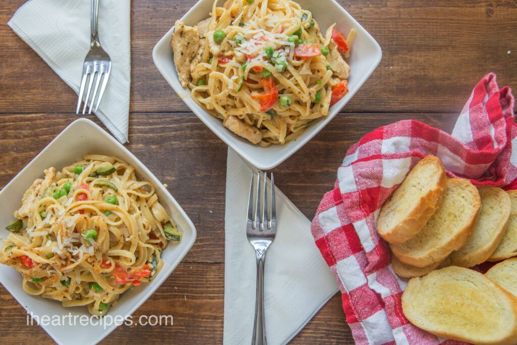 Two square white dishes filled with Lite Creamy Cajun Pasta sit on a dark wood table. Silver forks on top of white folded napkins lay next to each dish.  