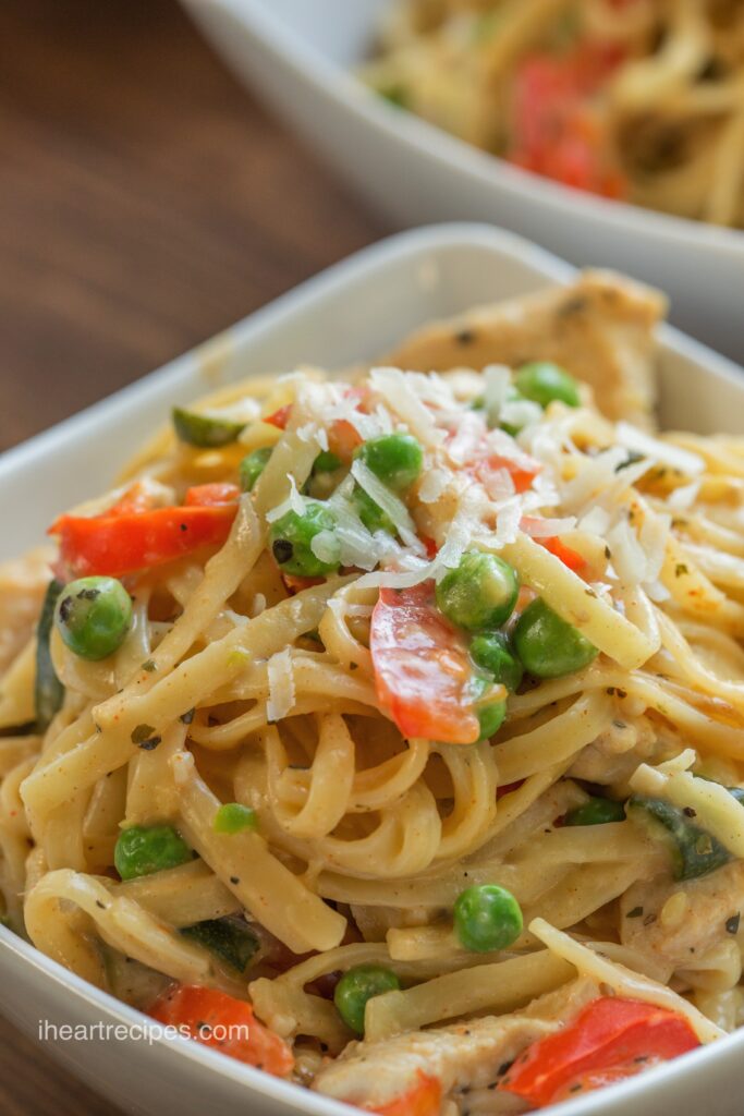 A close up image of golden pasta, tender chicken and bright veggies in a white dish. 