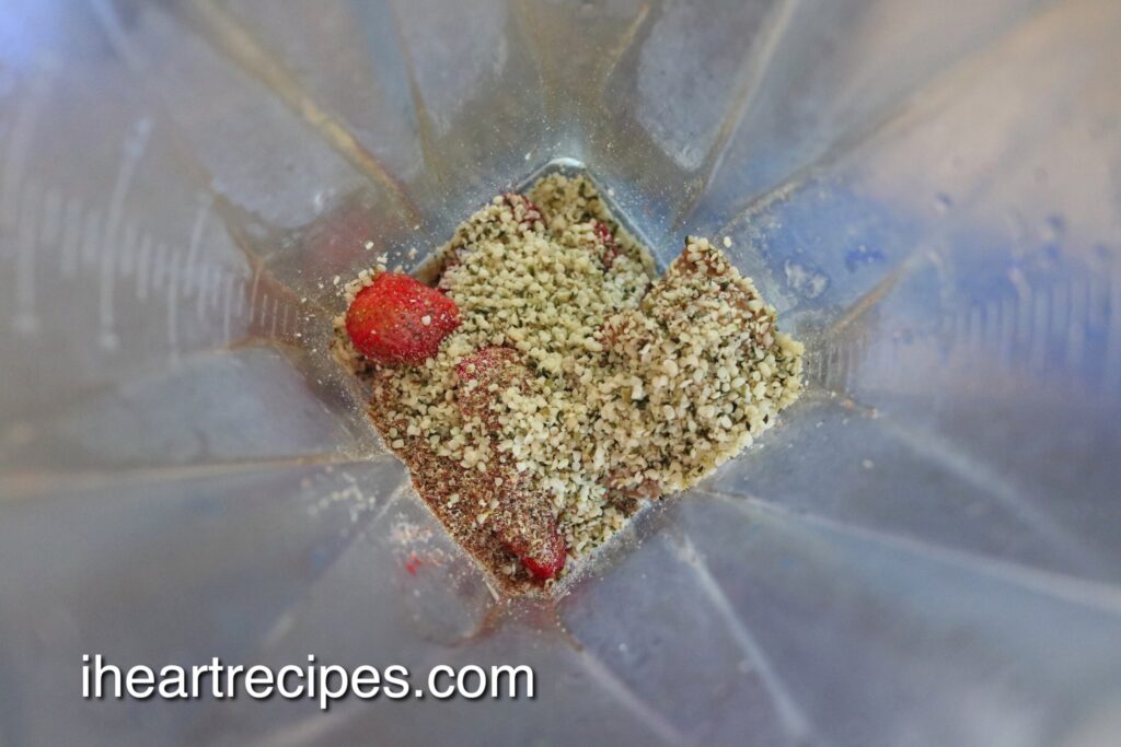 A view into a blender filled with flax seeds, hemp hearts and fresh strawberries. 