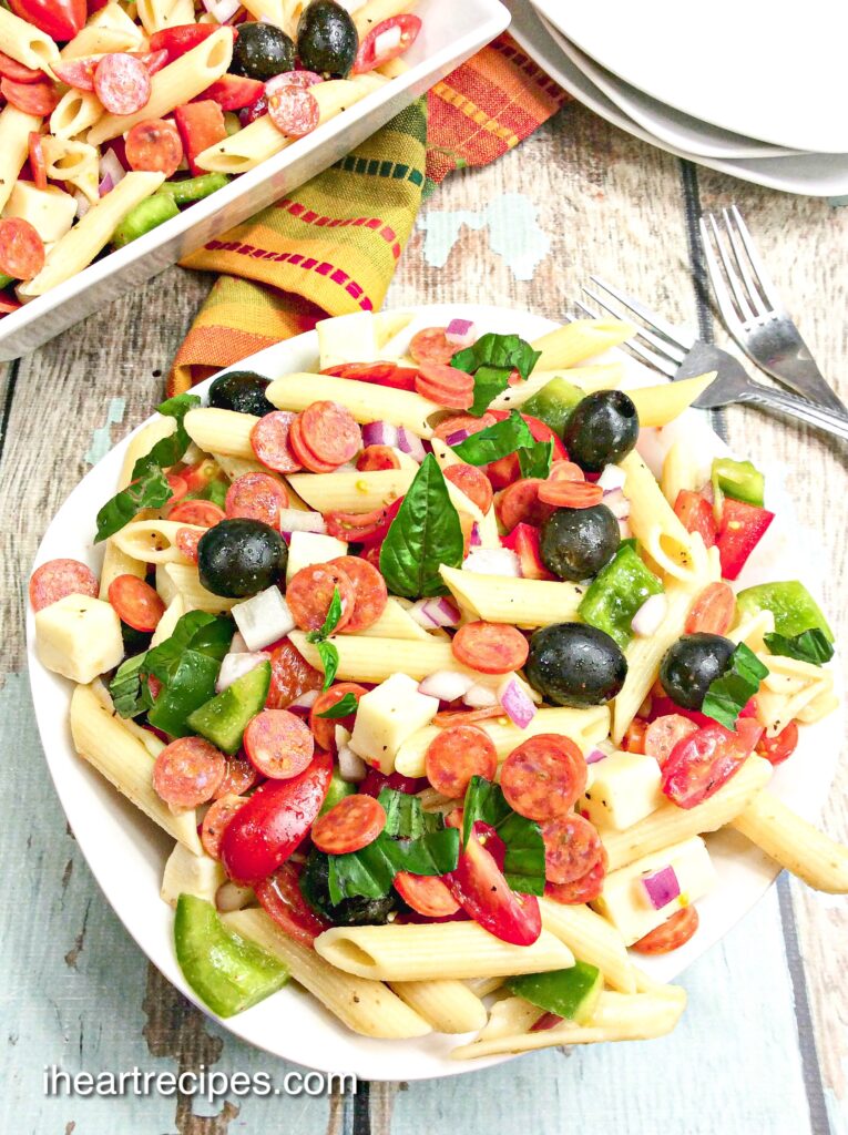 An overhead image of Pizza Pasta Salad in a white pasta dish served on a  rustic wooden table. 