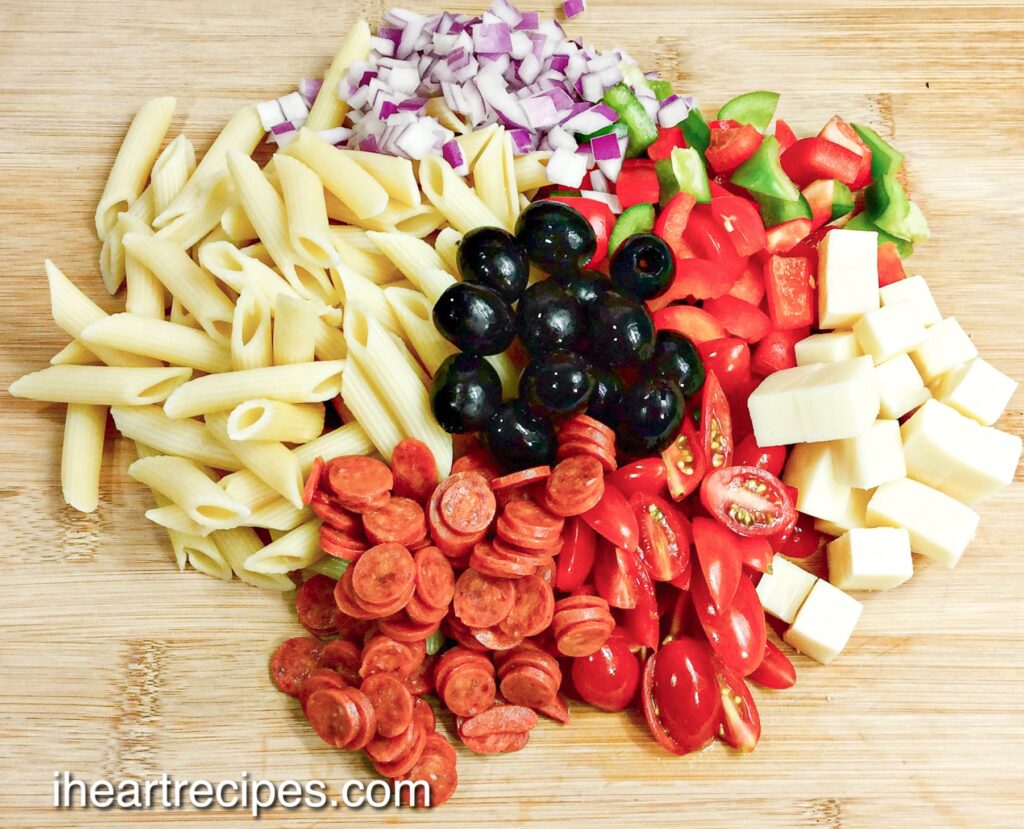 All of the ingredients for Pizza Pasta Salad arranged on a wood cutting board. 