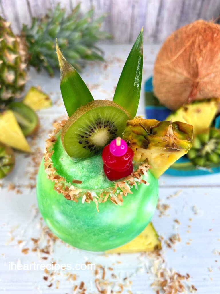 Bright green Kiwi Pina Colada in a glass garnished with toasted coconut and fresh fruit.