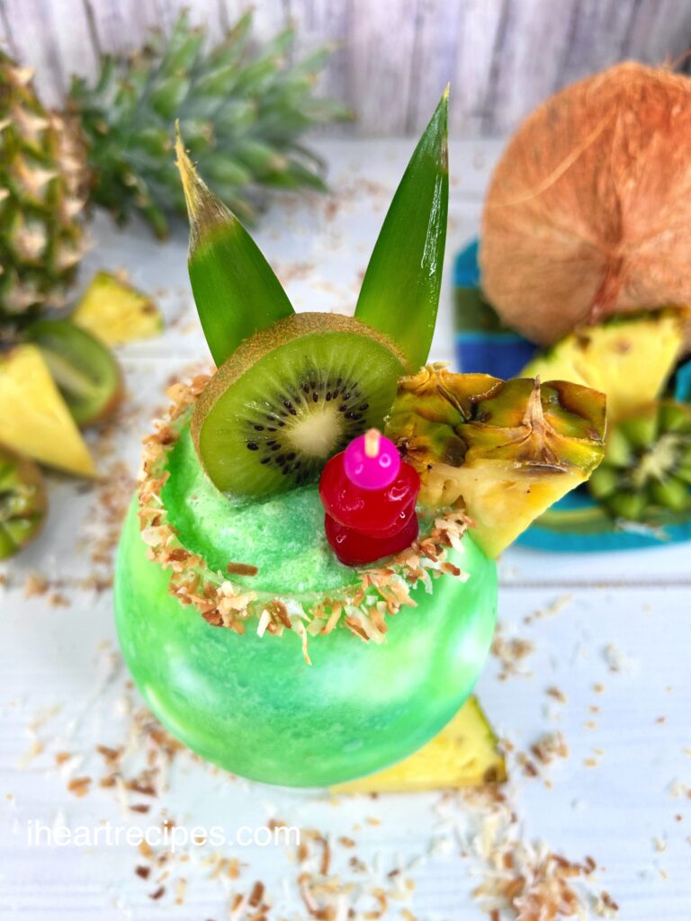 Bright green Kiwi Pina Colada in a glass garnished with toasted coconut and fresh fruit. 