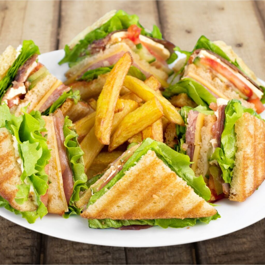 A quartered deli sandwich with meats, vegetables and Hellmann's mayo shares a round white plate with a stack of thick cut French fries.  