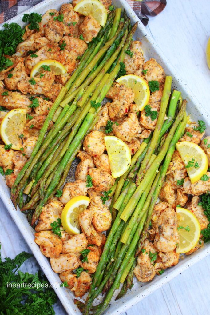 Alternating rows of asparagus stalks and seasoned chicken lay in a sheet pan. 