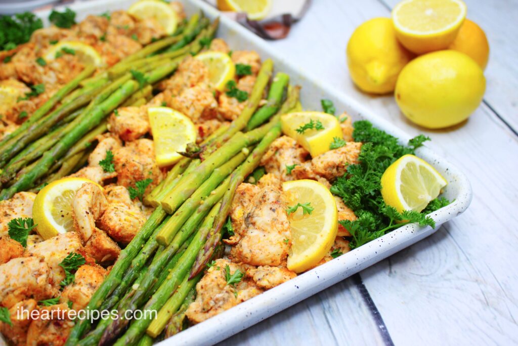 Rows of tender asparagus and savory chicken garnished with lemon wedges and fresh parsley line a sheet pan.
