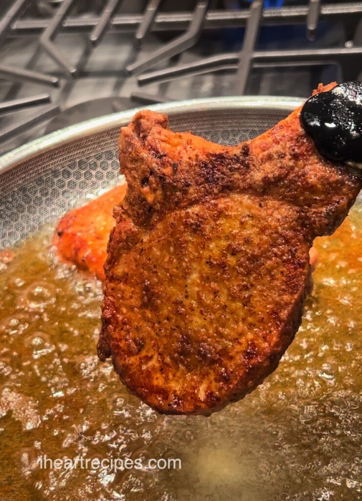 A golden fried pork chop held over a pan of bubbling oil.