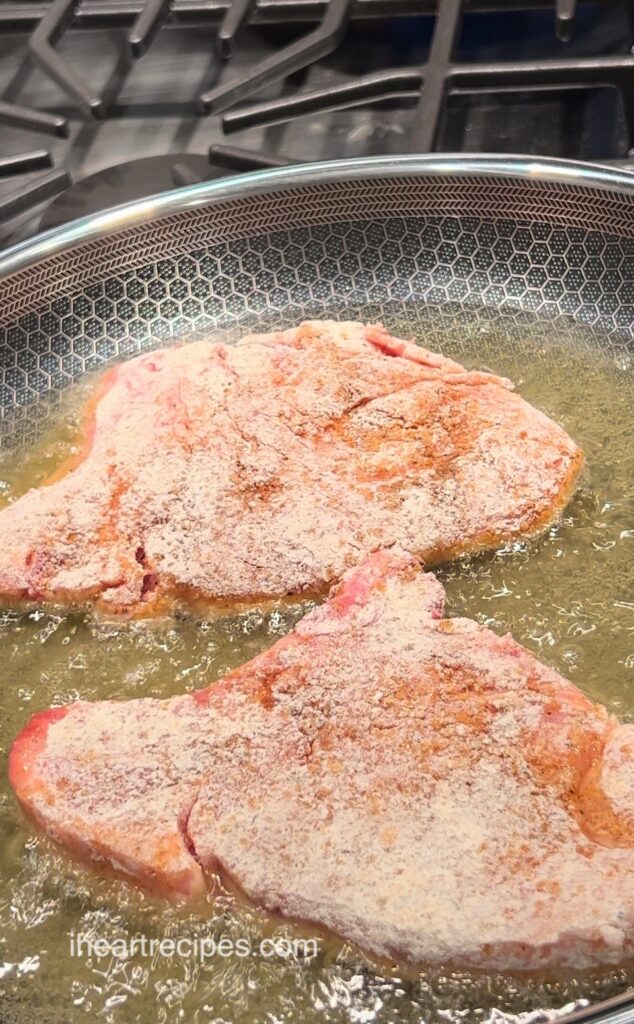Two floured Southern Fried Pork Chops in a pan of hot oil. 