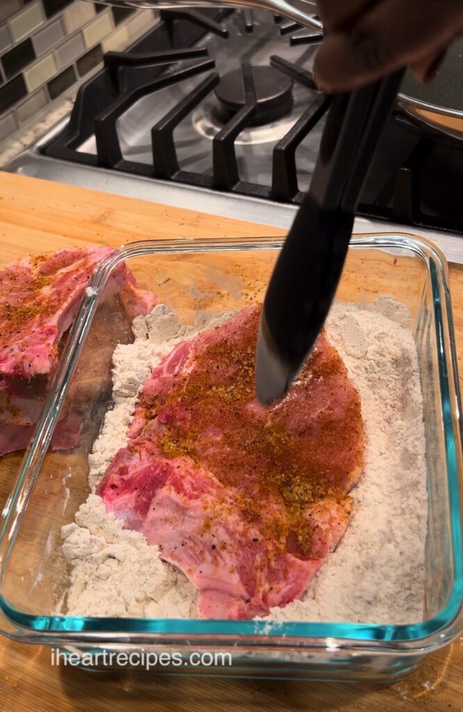 A seasoned pork chop being dredged in flour. 