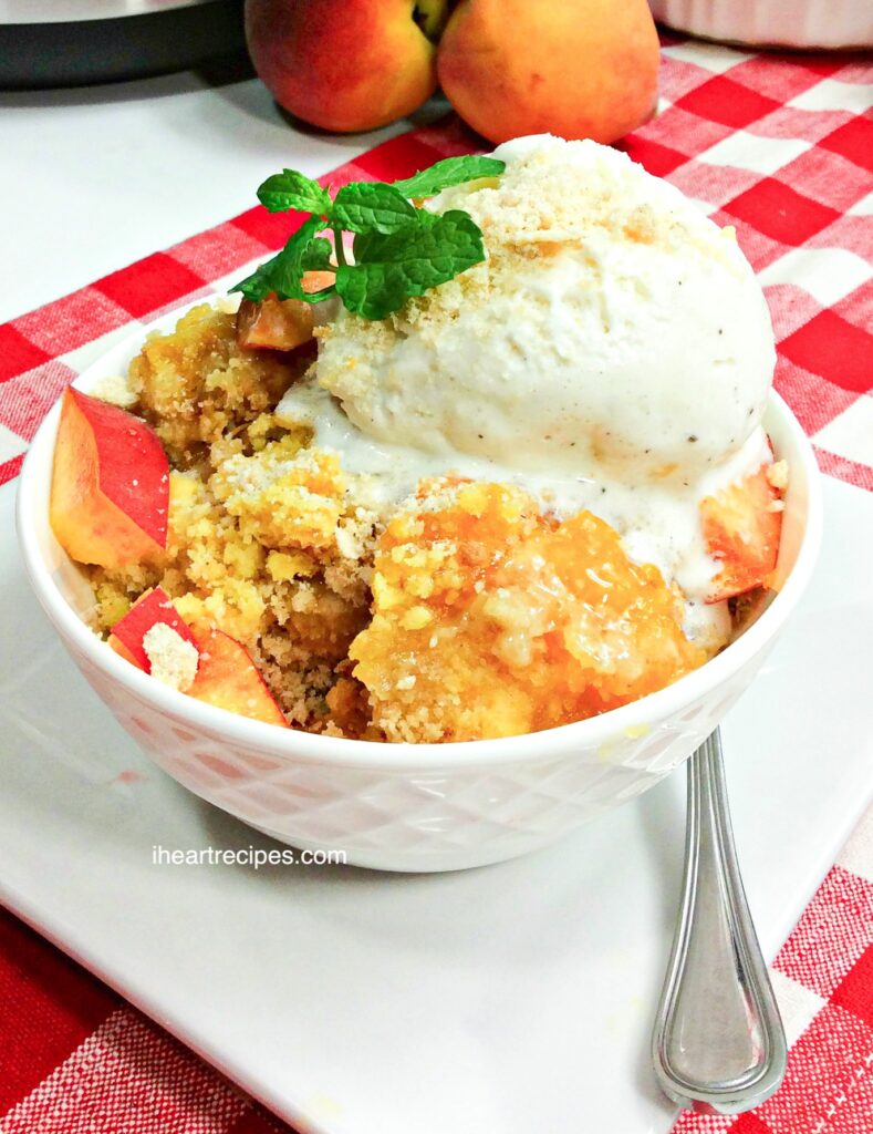 A round white bowl is filled with peach dump cake, pieces of peach and vanilla ice cream.
