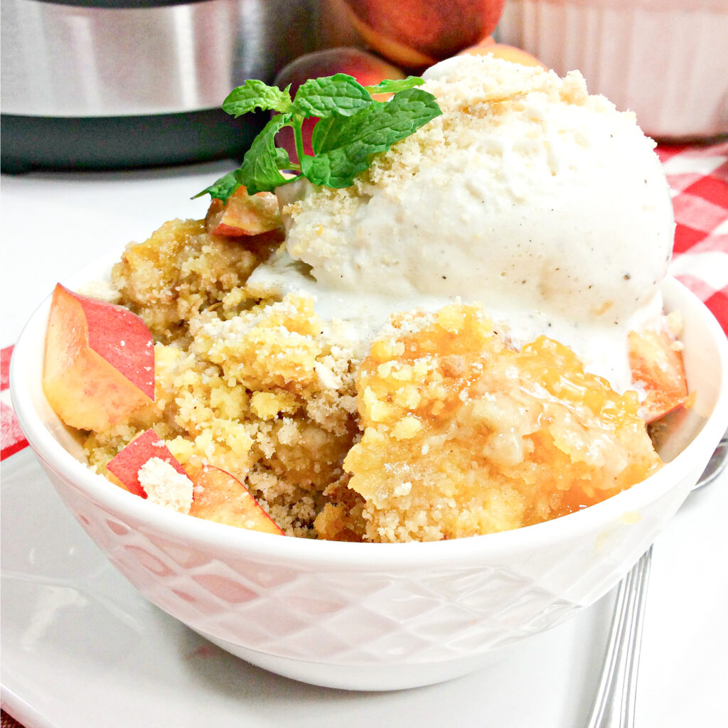 Crumbly, golden and moist peach dump cake fills a round white bowl. A scoop of vanilla ice cream sits on top of the cake. 