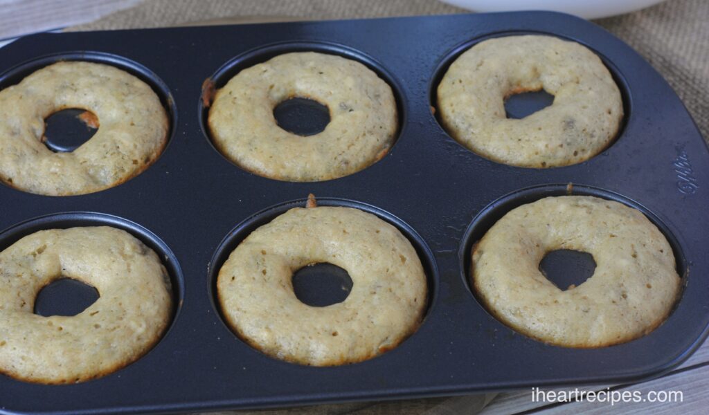 Six homemade banana bread donuts cool in a metal donut bake pan. 