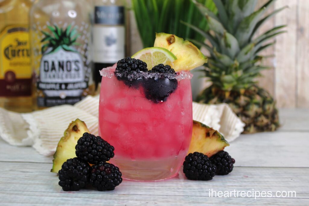 A frosty glass tumbler filled with bright pink Fruity Blackberry Margaritas garnished with fresh blackberries and slices of lime and pineapple.