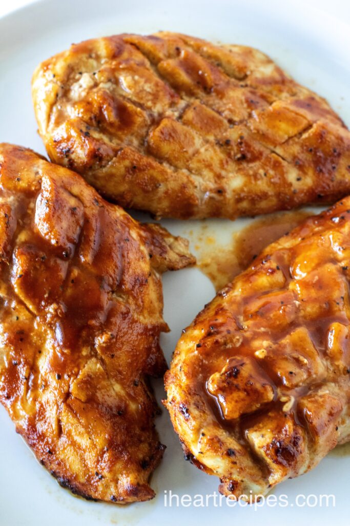 Three pieces of BBQ chicken on a white plate. Crisscross cuts are visible on the surface of each piece.