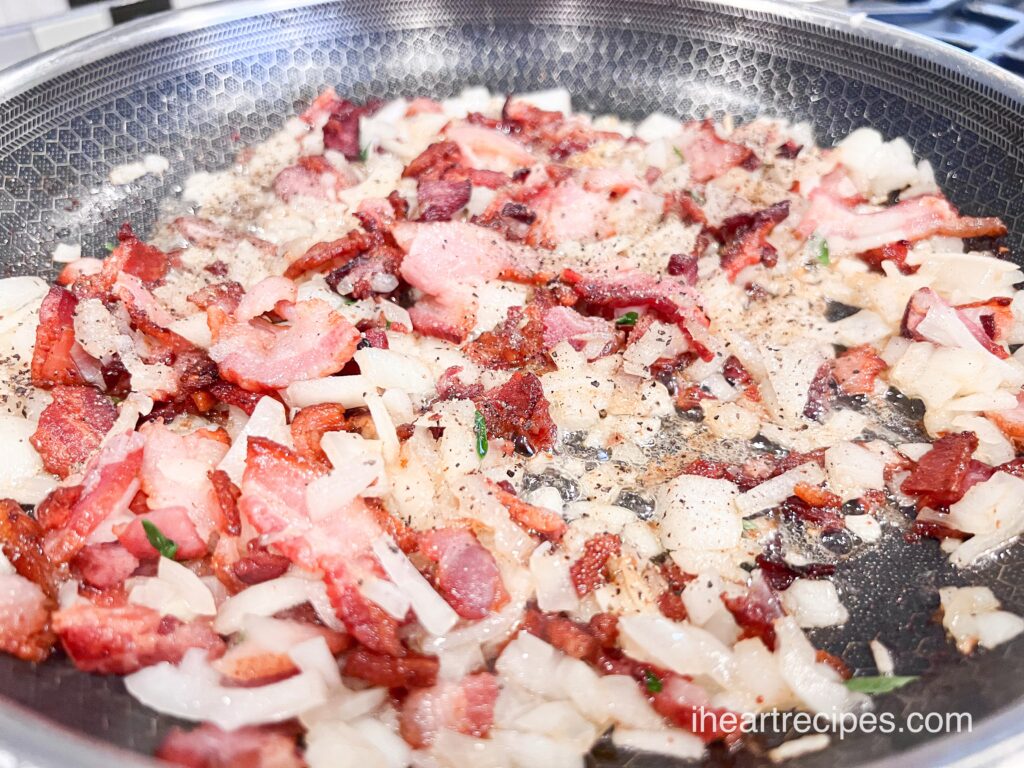 Softened diced onions, crisp bacon chunks and green herbs sautéing in a skillet. 