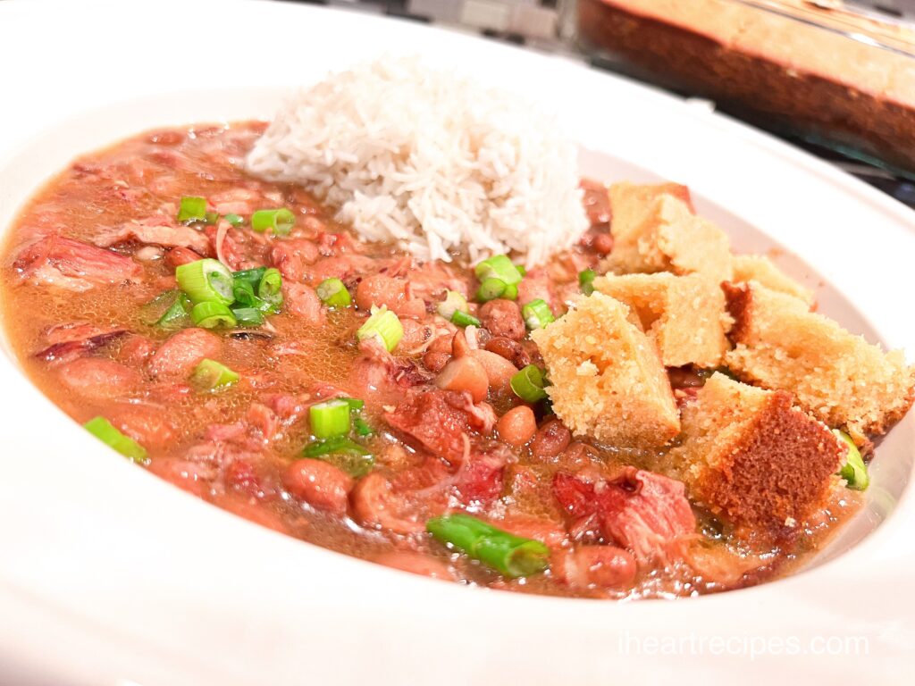 A shallow white bowl filled with southern pinto beans, a mound of rice and cubed corn bread. 