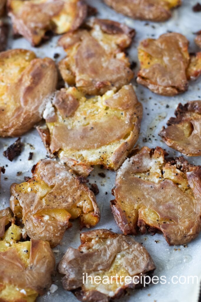 Golden and crispy smashed potatoes arranged on parchment paper. 