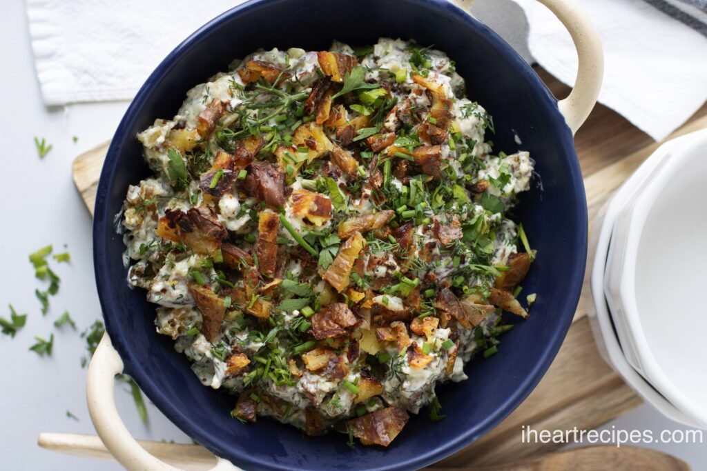 A blue bowl with white handles is filled with crispy smashed potato salad garnished with fresh herbs. 