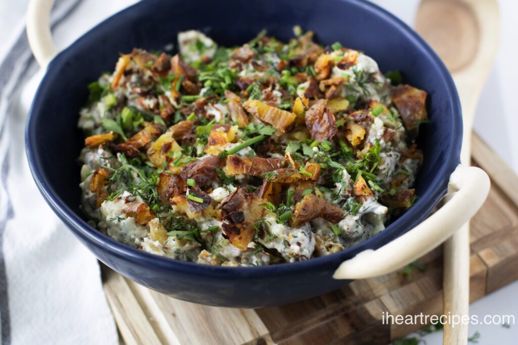 Creamy smashed potato salad sprinkled with fresh herbs fills a blue serving bowl. 