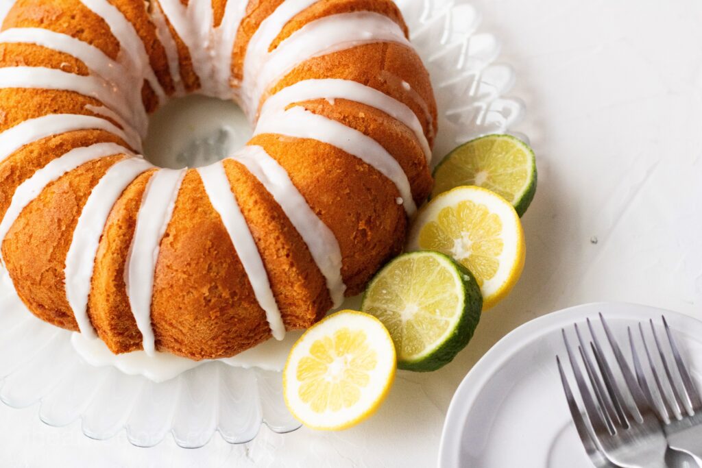 A homemade 7up cake with icing on a cake platter with lemon and lime slices.