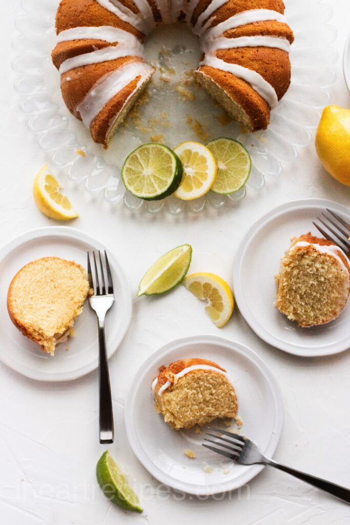  A cake on a platter with lemon and lime slices, and two slices of cake on plates.