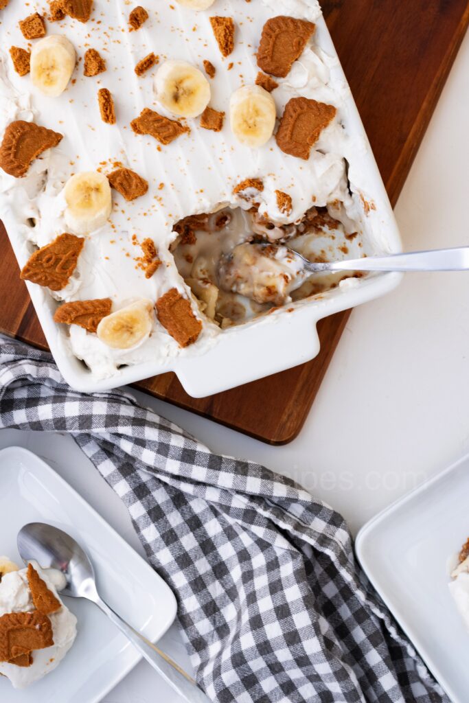 A white dish with vegan banana pudding, topped with whipped cream and crushed cookies.