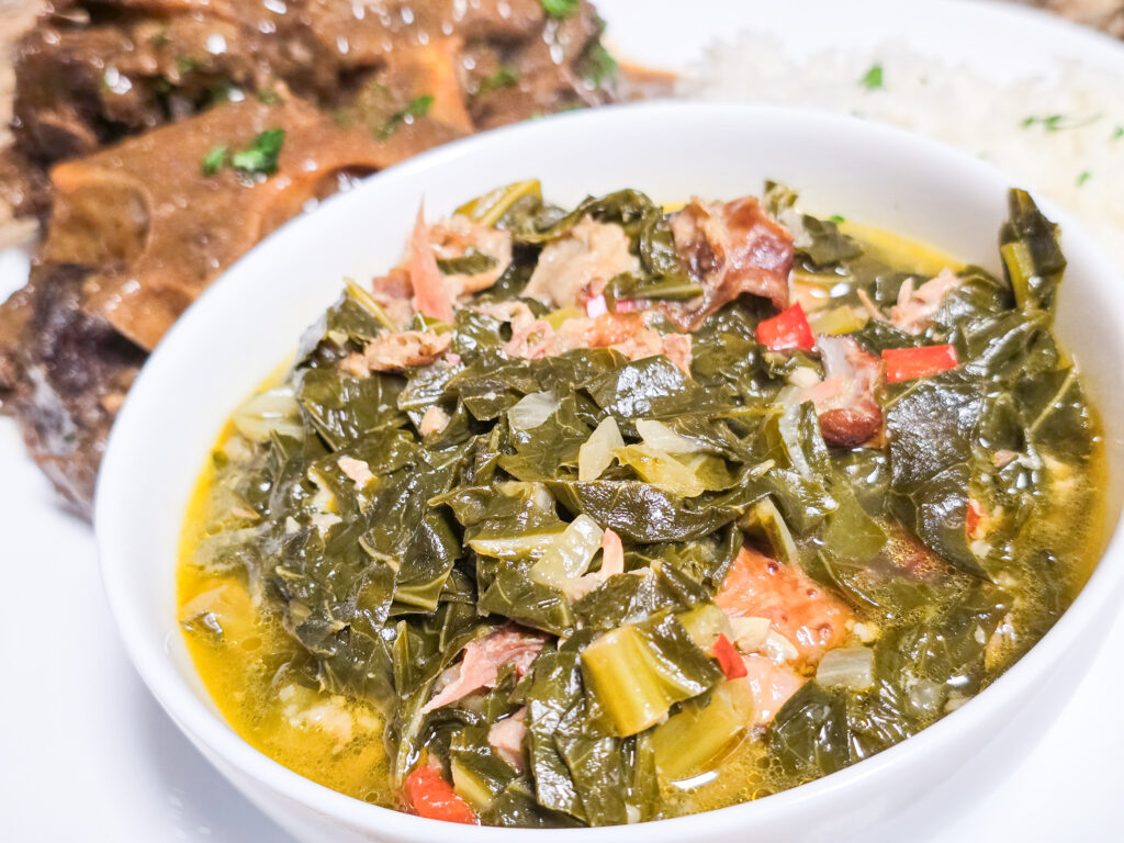 Southern collard greens with smoked turkey and red peppers in a bowl. Smothered beef neck bones in the back of the bowl.