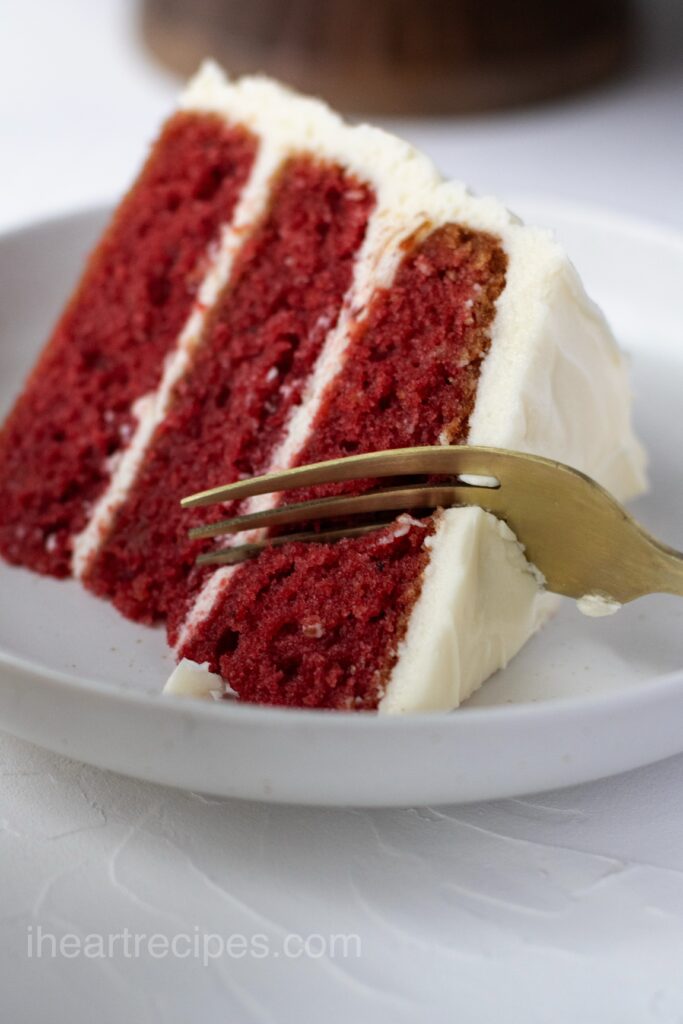 Three layer Red velvet Cake with a golden fork cutting into it.