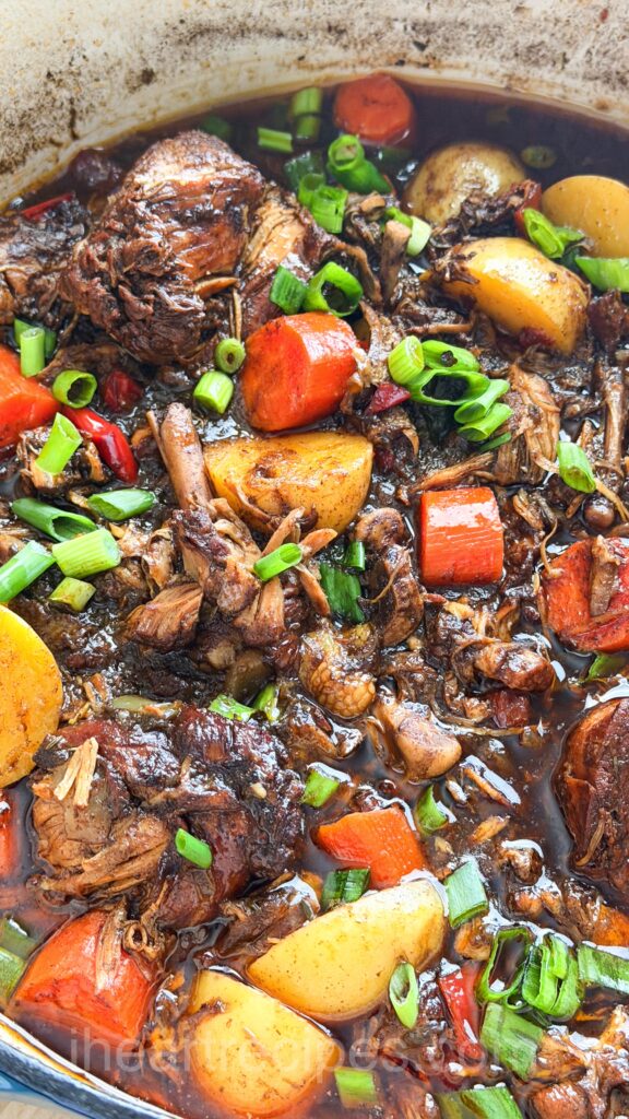 brown stew chicken and potatoes, with carrots in a pot.