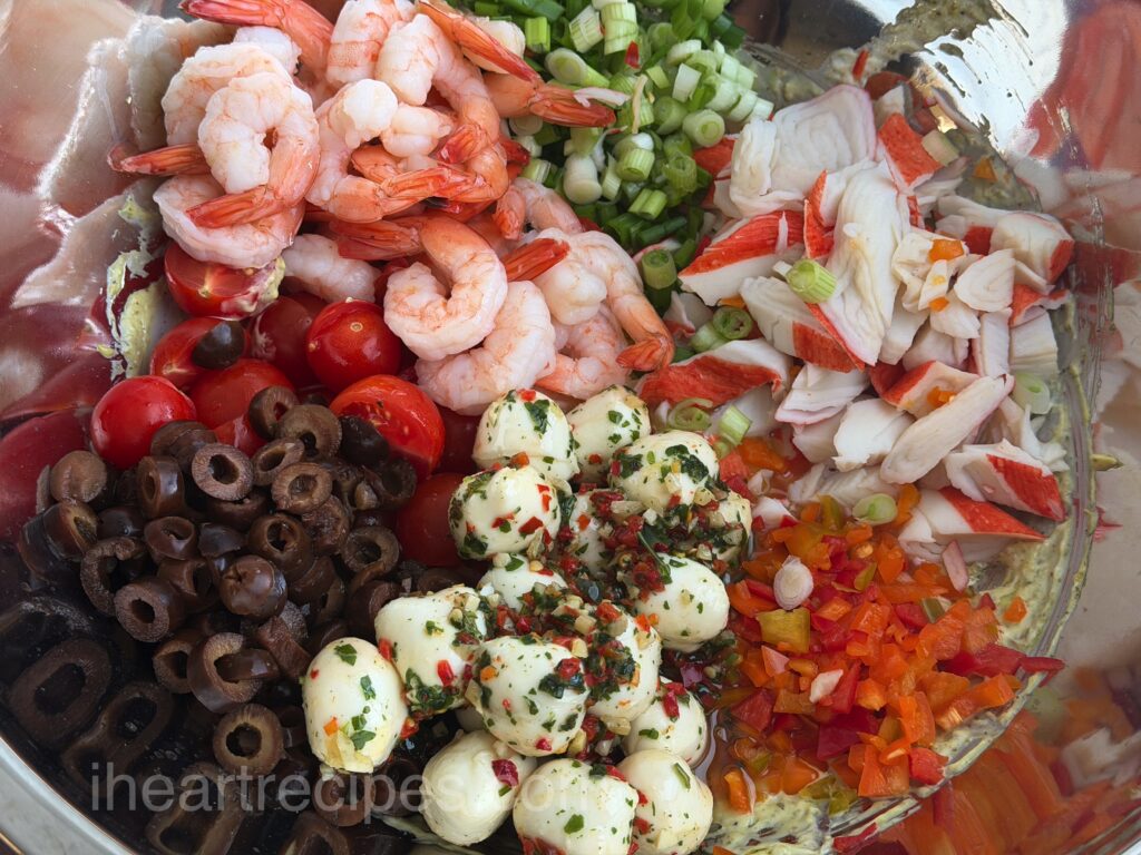 shrimp, imitation crab, green onions, sliced tomatoes, mozzarella, onions, and more in a large mixing bowl.